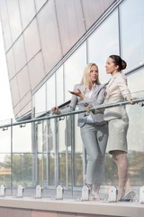 Full length of young businesswomen conversing at office balcony