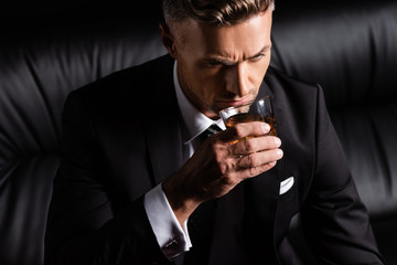 Businessman drinking whiskey on couch isolated on black