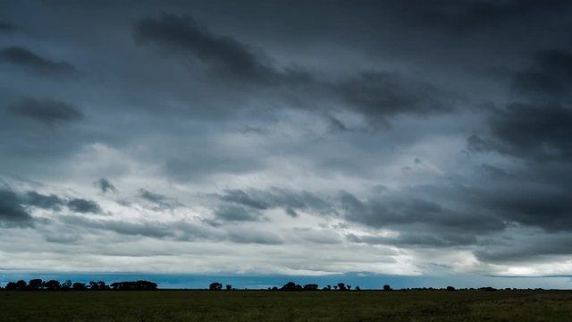 Static timelapse of dark and dramatic clouds rolling in with a thunderstorm and lightning over a rural farm land, scenic landscape, South Africa, while starting to rain.