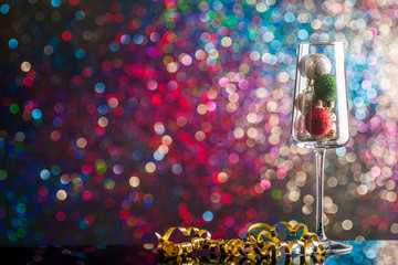 A glass of champagne filled with Christmas decorations against the background of colorful lights.