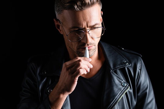 KYIV, UKRAINE - OCTOBER 11, 2019: Handsome pensive man smoking iqos isolated on black