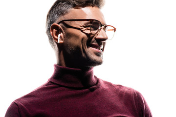 Obraz premium Smiling man in wireless earphones and eyeglasses looking away isolated on white