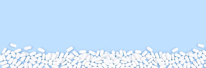 Blue monochrome border of pile of pills tablets on the table. Flat lay long banner. Healthcare and...