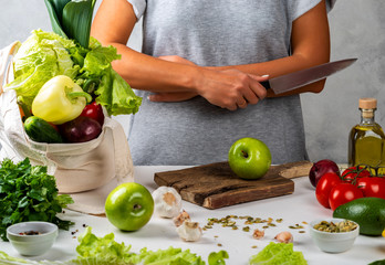 Woman holds knife and is going to cook a healthy diet food with a cotton eco bag full of fresh vegetables on the table.