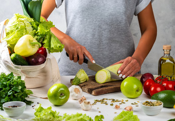 Woman cuts a squash and cooking a healthy diet food with a cotton eco bag full of fresh vegetables on the table.