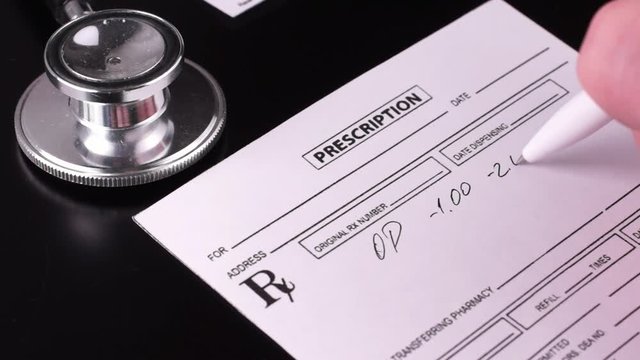 Physician fills a prescription with a white pen on a dark background next to a phonendoscope. Close-up