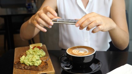 Woman Hands Taking Picture Of Coffee And Avocado Toast With Smartphone