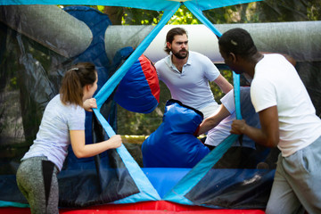 Gambling friends boxing giant gloves on an inflatable trampoline in an amusement park