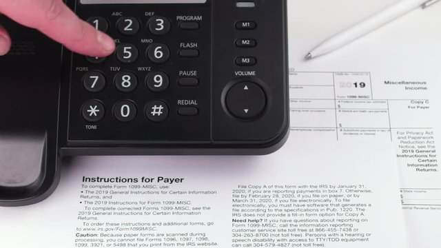 A person dials a phone number against the background of instruction for the payer, tax form 1099 and a pen. Macro video