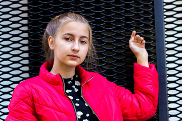 Beautiful teenager girl on a background of a city street in a bright red jacket.