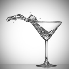 Clear cocktail splash out of glass with ice cube.