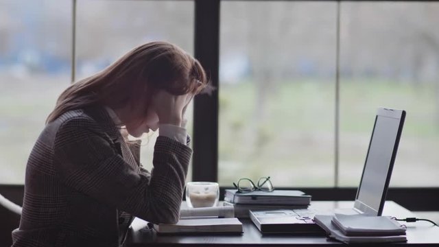 portrait of a tired girl, business woman is nervous because of the hard work online sitting at table by window in an expensive restaurant during coffee break