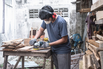 Carpenter polishing plank wood using circular sander on grinder power tool at outdoor workshop.