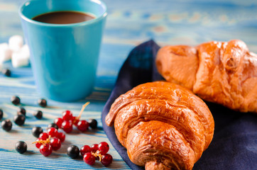 French breakfast: Ruddy croissants with forest berries and a cup of coffee with milk stand on a table