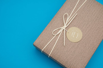 A gift box isolated over turquoise background with copy space. Box is tied with a cord with a label with Wishes and Happiness. Holiday, birthday, New Year and Christmas gift concept. Selective focus. 