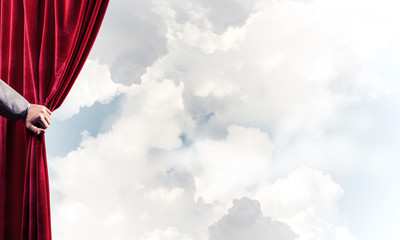 Cloudy landscape behind red curtain and hand holding it