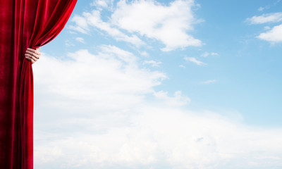 Cloudy landscape behind red curtain and hand holding it