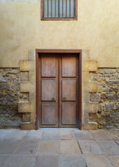 Facade of old abandoned stone bricks wall with decorated wooden door and wrought iron window above