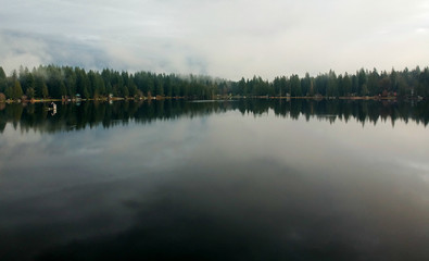 Lovely Lake Joy and the waterfront houses on a fog covered day with the surrounding trees and lingering clouds above reflecting in the water in the pacific northwest.