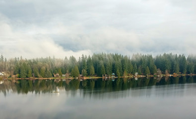 Lovely Lake Joy and the waterfront houses on a fog covered day with the surrounding trees and lingering clouds above reflecting in the water in the pacific northwest.