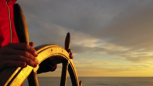 Captain holding ship rudder and steers in sunset light.