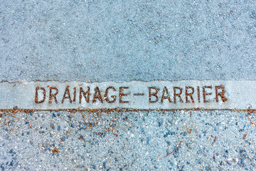Drainage barrier sign on concrete slab between asphalt pavement indicates the border of urban storm drainage system