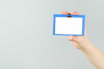 Female hand holding blank white bagde on grey background