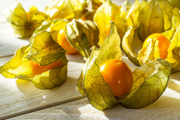 Many yellow ripe physalis fruits (Physalis peruviana) in the sunshine on a white wooden table. Fruits and vegetables, vegetarian and healthy eating. Ready to eat.
