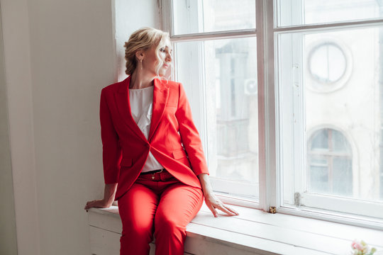 Portrait Of A Beautiful Blonde Woman In A Red Business Suit In The Office