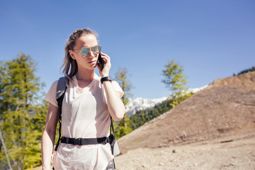 Slim young female traveler with a backpack got to the destination of the trip calls on the smartphone Wireless internet concept in nature. The ability to communicate by phone and good cellular