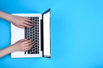 Fototapeta na wymiar Female hands typing on laptop keyboard on blue background
