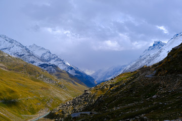 Fototapeta premium Beautiful view of the mountains covered with greenery and snow-capped peaks between which the river flows and winds the road. 