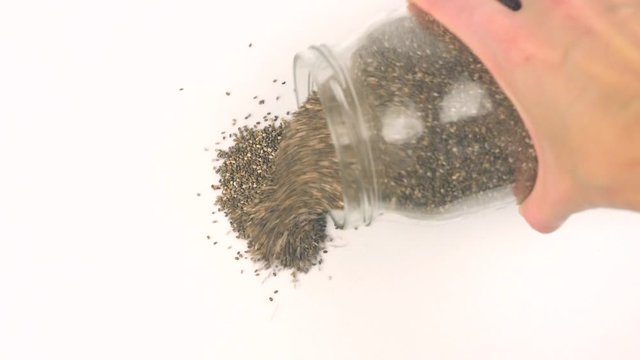 Closeup view pouring black chia seeds from glass jar