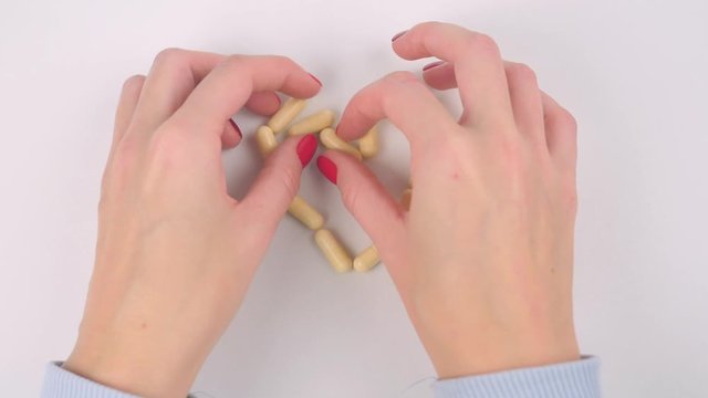 Woman's hands making heart shape yellow capsule pills on white table