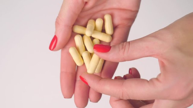 Woman's hand gives yellow capsule pills and takes one with other hand