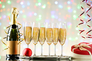 Bottle, glasses of champagne with gift box and bauble on blurred lights background