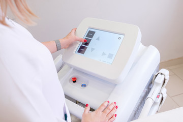 Rear view of a female beautician in white coat presses on display of device to select desired procedure. Concept of modern high-tech equipment for anti-aging procedures. medical examination of patient