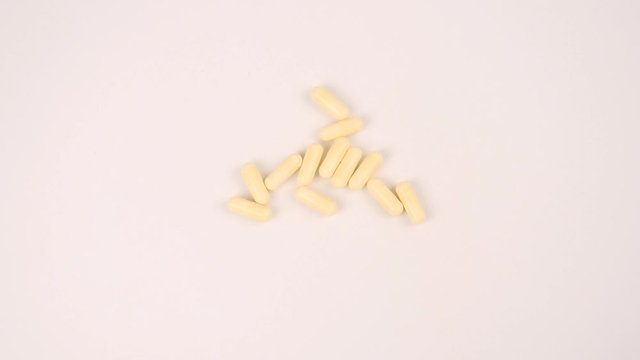 Woman's hand putting yellow capsule pills on white table