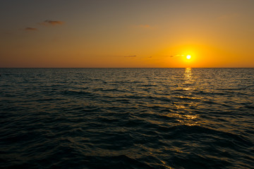susnet over the ocean, the light is reflecting in the sea while the sun sets farway on the horizon 