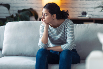 Boring young woman looking to side and thinking while sitting on the sofa at home.