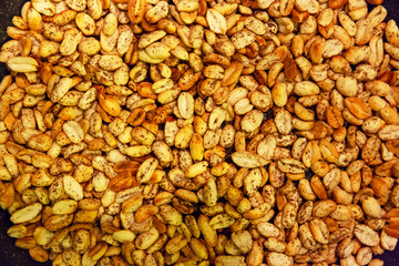 Roasted peanuts shades of yellow and brown, sprinkled with pepper appetizing appearance lies in the kitchen on a black pan.