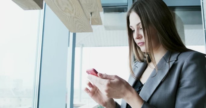 Portrait of young attractive woman looking at smartphone on the office near bif window
