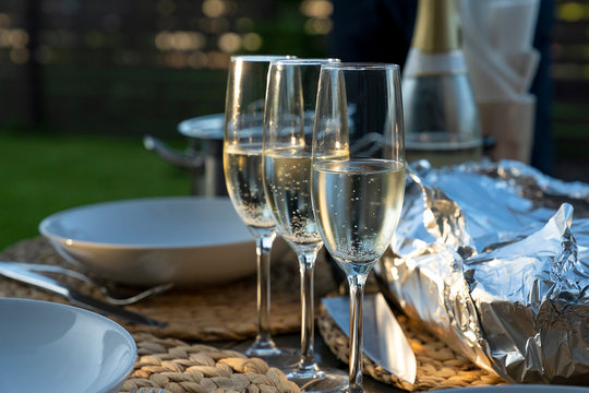 Sparkling white wine glasses and foil wrapped barbecue on a table. Dinner party at homes  terrace.