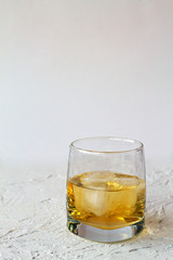 glass of whiskey with ice on white table. glass of lemonade or cocktail with pieces of ice on a white background. vertical