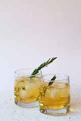 cold drinks. glass of whiskey with ice and slices of orange on white table. two glasses of lemonade or cocktail with pieces of ice and a sprig of rosemary on a white background.