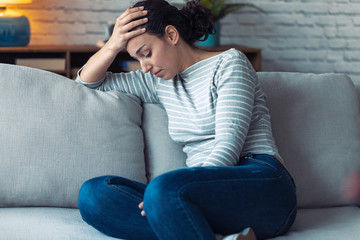 Depressed young woman thinking about her problems while sitting on the sofa at home.