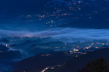 Naklejka na ściany i meble Night lights of villages with patches of fog in the Bregenzerwald. Vorarlberg, Austria