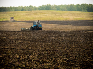Tractors plow plowland on an autumn clear day