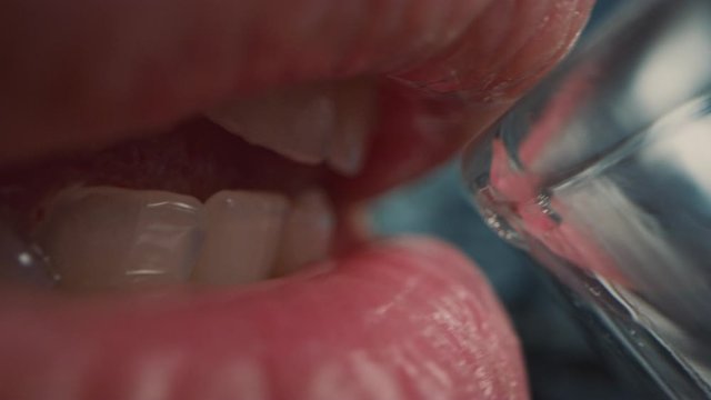 Extreme Close Up Macro Shot of a Person Drinking Water from a Transparent Glass. Fresh Tap Water Flows Inside the Mouth. Natural Mouth with Perfect White Teeth and Red Lips.