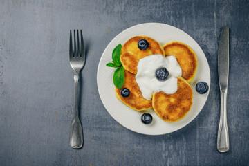 Pancakes with fresh blueberries, mint and sour cream on white plate. Healthy breakfast food. Table top view. Grey background